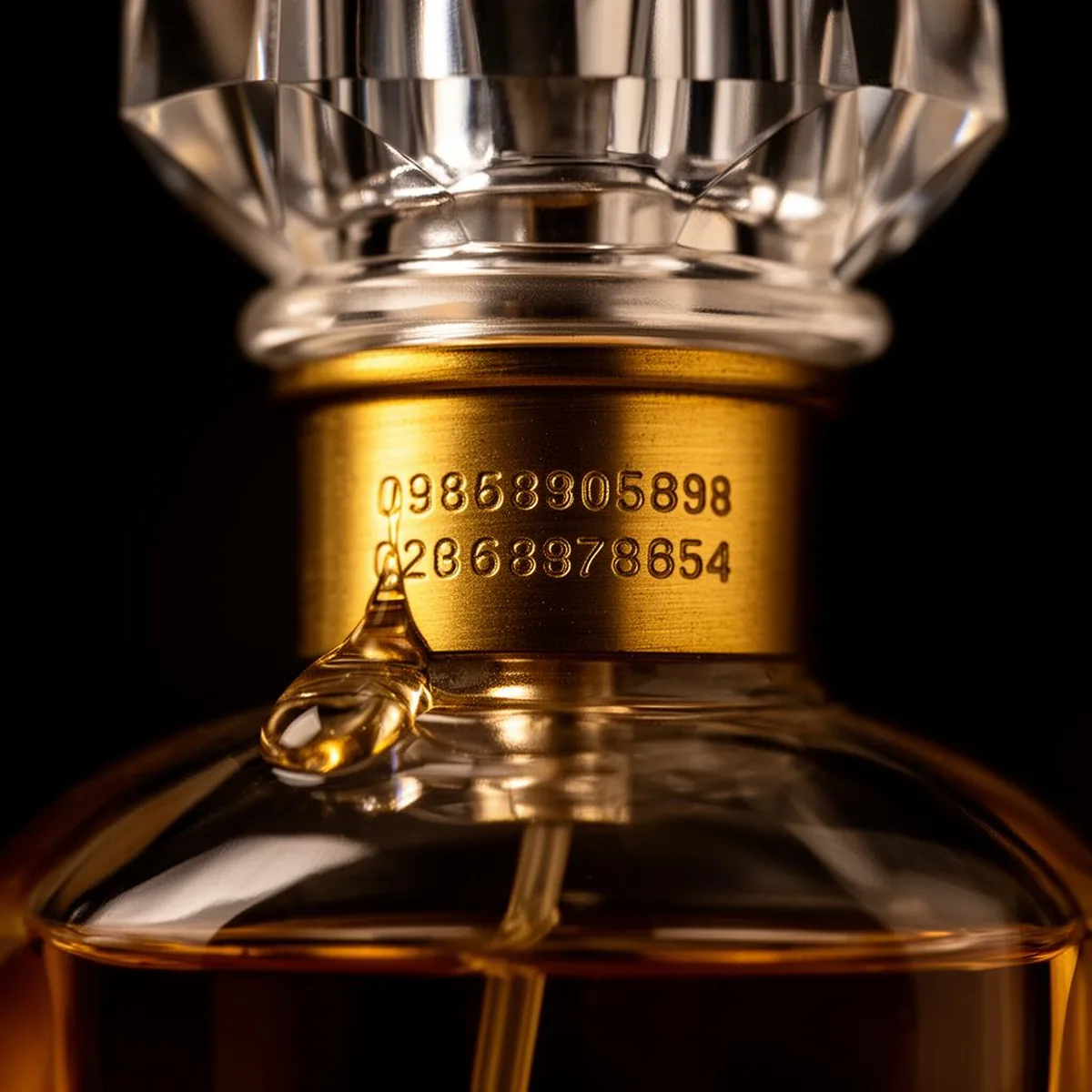 Macro detalle del cuello dorado y código grabado de un frasco de perfume original con una gota cristalina.